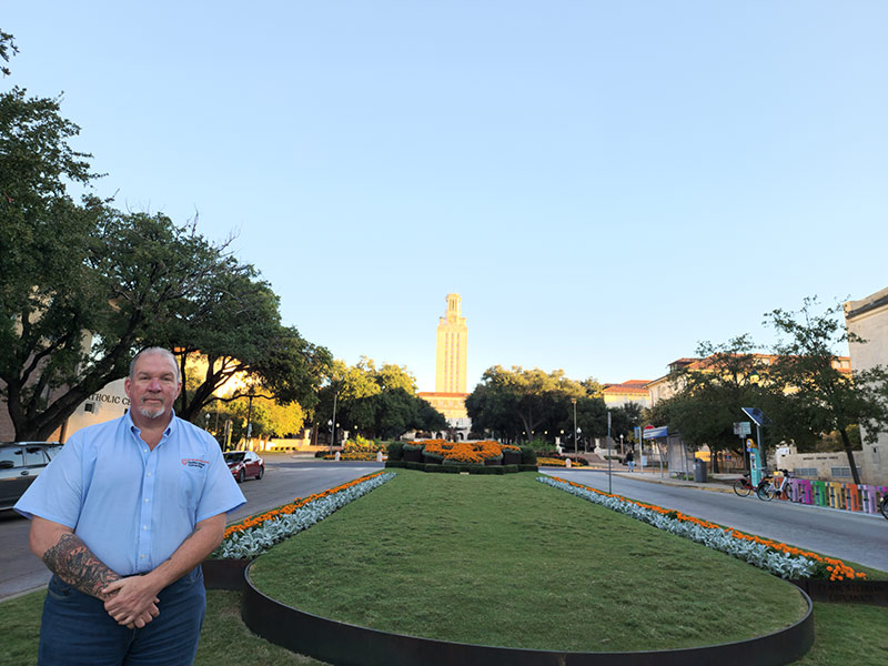 Member of UT Irrigation crew in front of lawn and UT tower